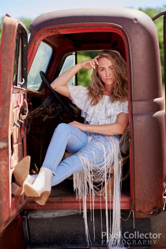 Lounging in her old truck with her feet on the door.