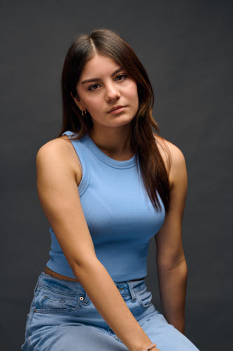Headshot of young woman sitting on a stool with a pensive expression.